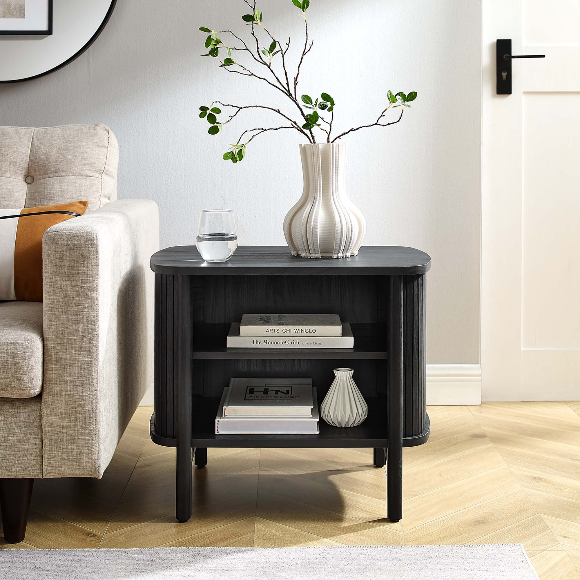 Cadence Open Fluted Nightstand in Black - styled as a side table beside a sofa, with a vase on top and books on the open shelves